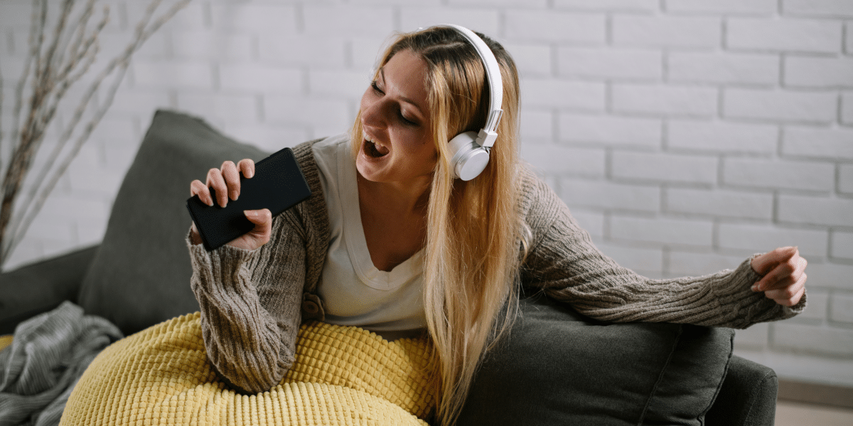 woman listening to music with her headphones and singing with a tv remote in her hand